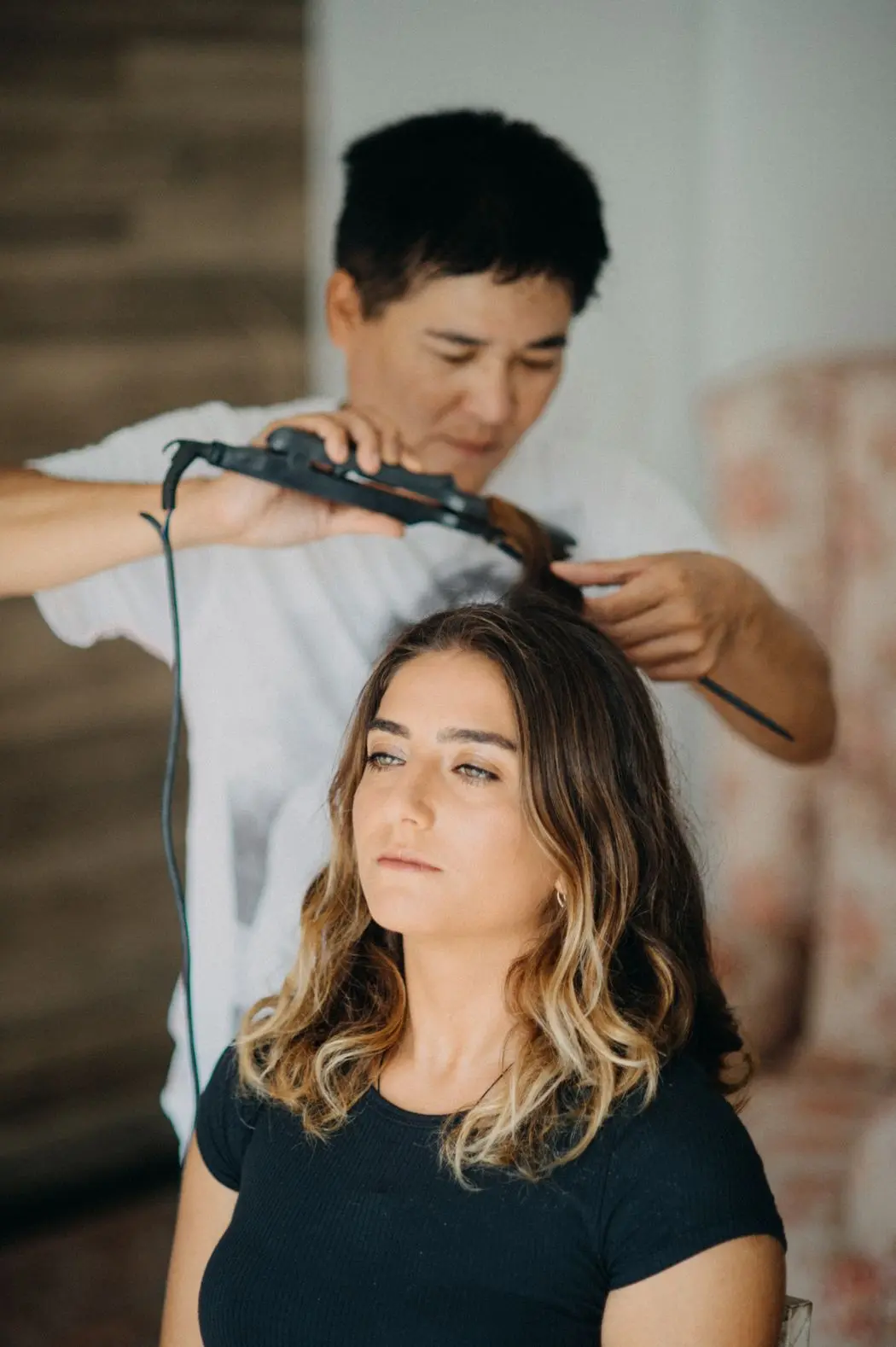 A stylist curling a client’s hair in a calm, sunlit salon